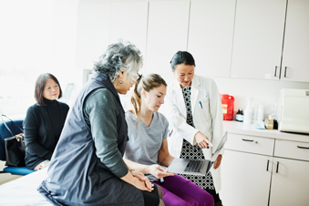 Elderly patient speaking to providers in an exam room at a clinic.