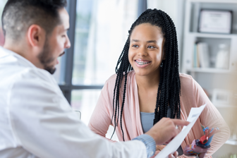 Female adolescent is seated and listening to her male doctor in the clinic office