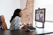 A female is sitting and smiling at her computer speaking to people in the video conference.