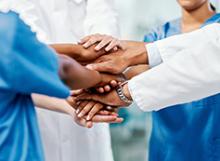 Group of Clinicians Huddled together with hands in a teamwork pose.
